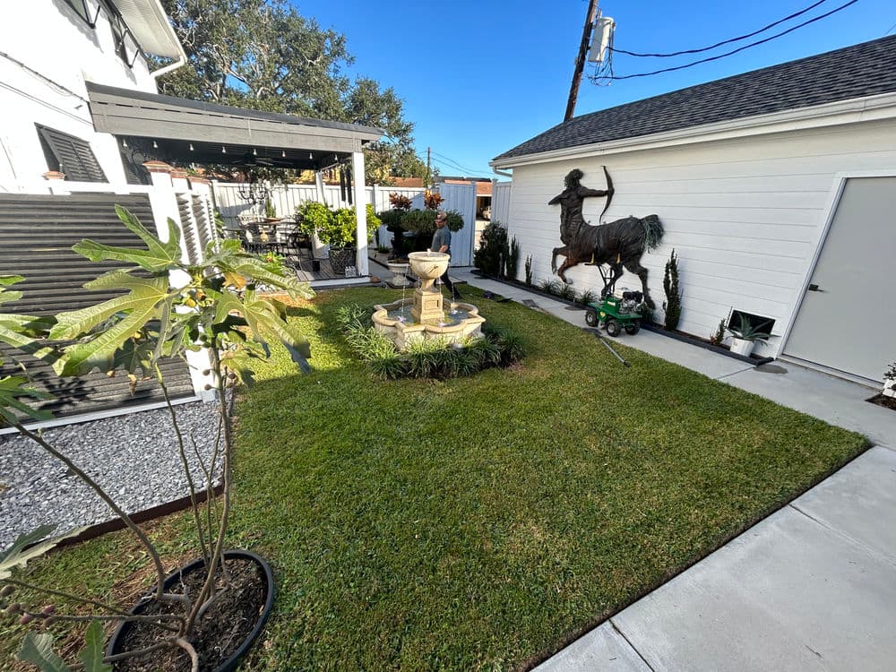 Lush backyard garden featuring a fountain, sculpture, and landscaped areas with patio.