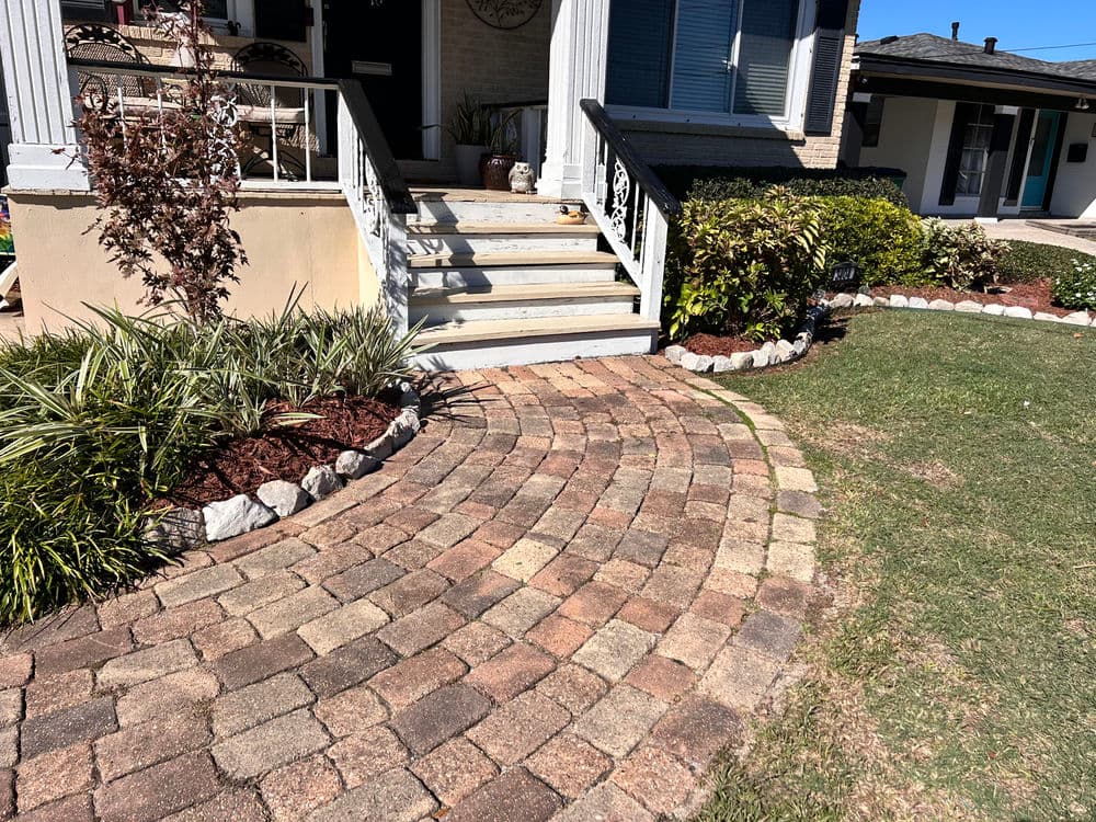 Curved brick walkway leading to a home entrance with landscaped borders and steps.