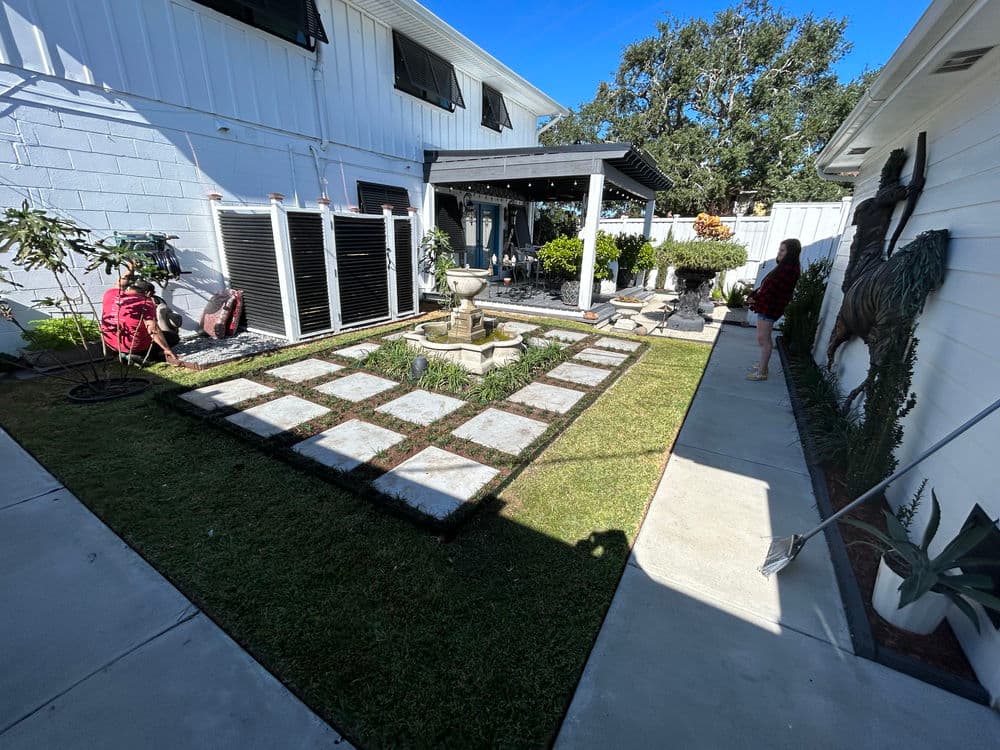 Landscape design featuring a stone patio, fountain, and lush greenery in a residential backyard.