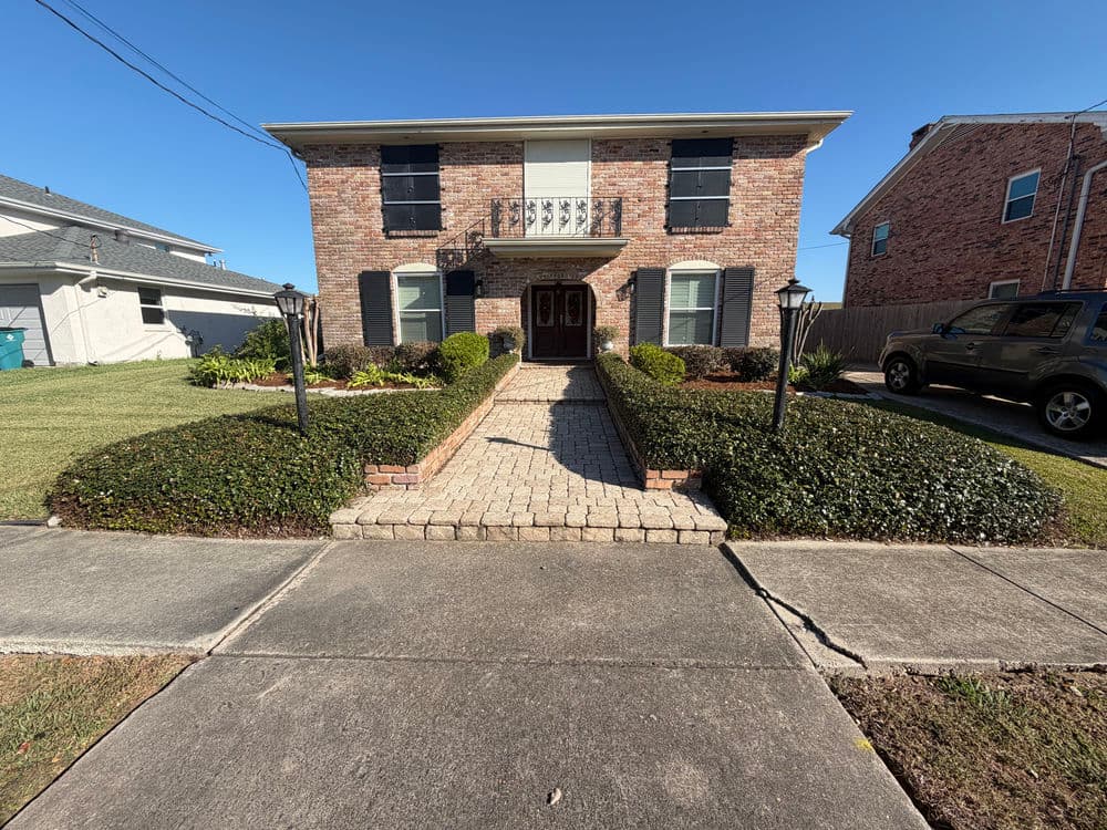 Brick house with a front walkway, garden, and landscaping on a sunny day.