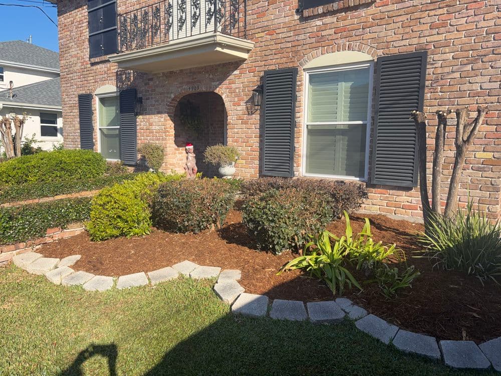 Lush front yard landscaping with brick home, bushes, and stone edging under clear blue sky.